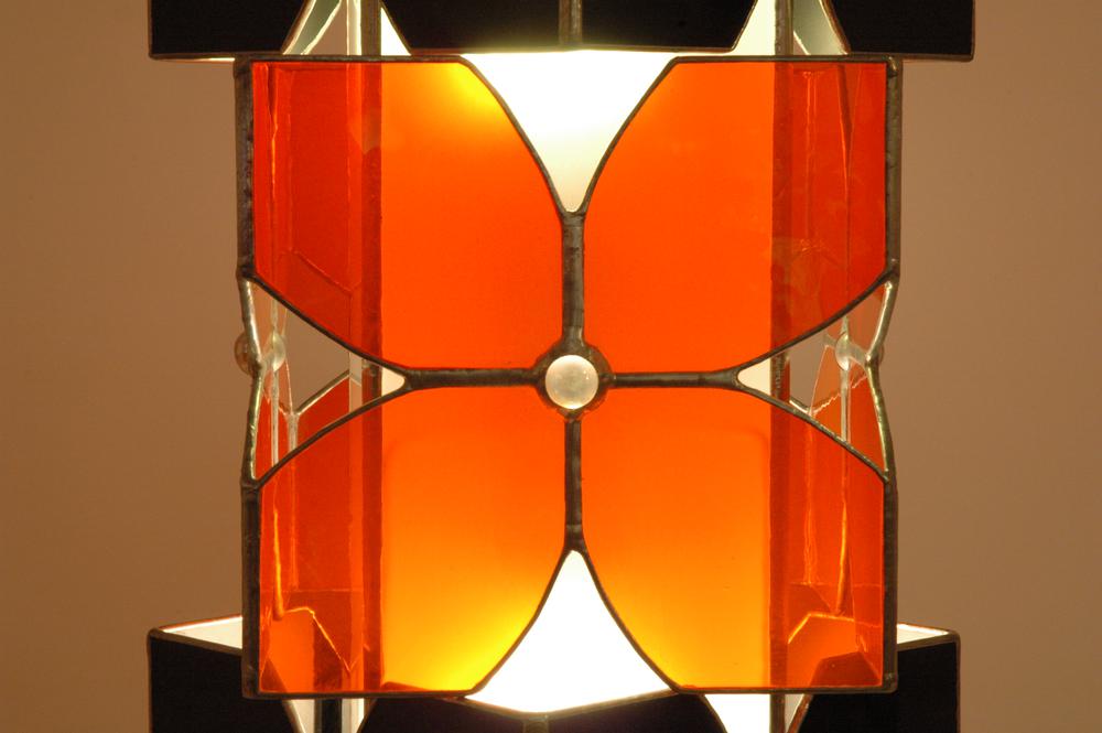 Vitraux oranges et noirs pour cette lampe à poser. Equipée de deux ampoules elle constitue une source de lumière intéressante en lampe d'appoint intégrée à la déco, sur un bureau ou une table de chevet.